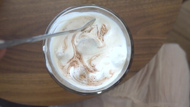Woman stirs iced coffee with salt in a cozy cafe