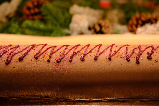 Close-up of a rolled cake decorated with jam, with pine branches and pinecones in the background