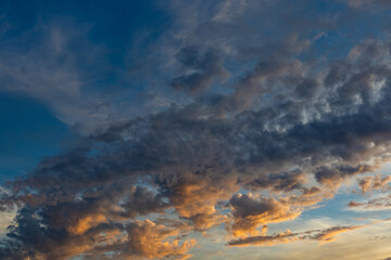 Obraz premium Dramatic sunset cloud formations illuminated by golden orange light against a deep blue sky