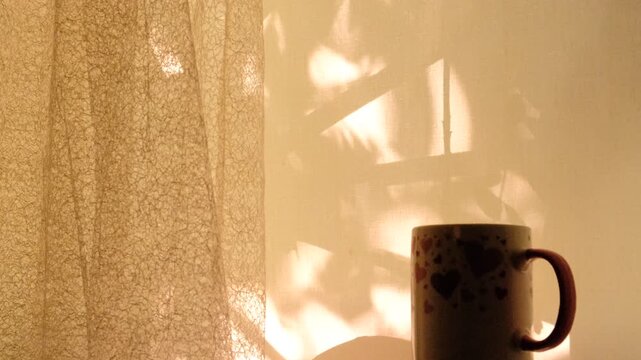 Cup of tea or coffee at the morning, Light and floral shadow, soft blurred sunlight flares. Vintage textile background. Abstract backdrop with crossed lines shadows. Wabi sabi style aesthetics.