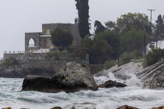 Dramatic coastal landscape with a stone house and crashing waves during a rainy stormy day