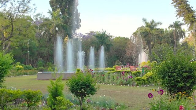 Wide Angle View Of Active Water Fountains And Blooming Flower Beds In Lush Botanical Garden