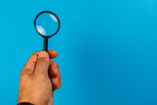 Hand holds a magnifying glass on a blue background for inspection