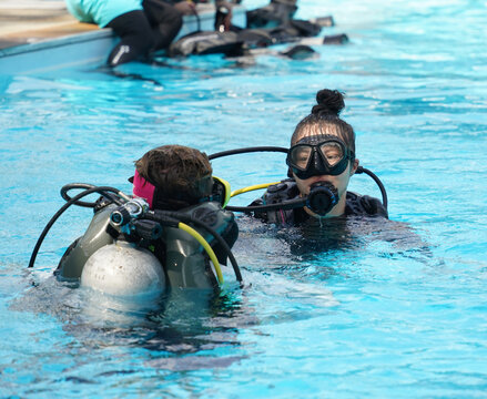 A professional diver and a novice practice diving in a pool.
