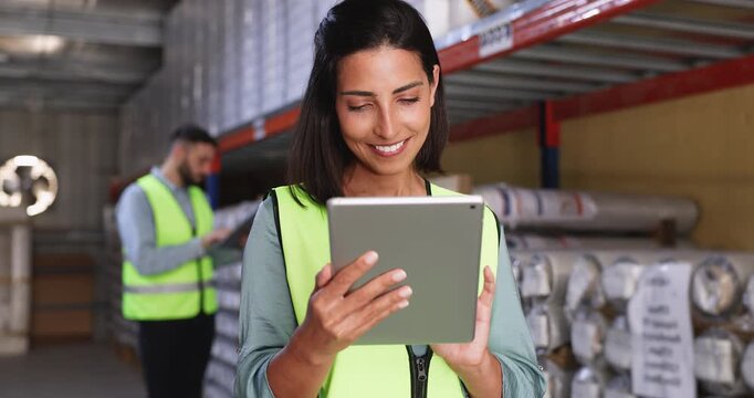 Positive young Latin storage supervisor woman in yellow vest using logistic application on tablet for inventory control, counting boxes on metal shelves, typing on gadget