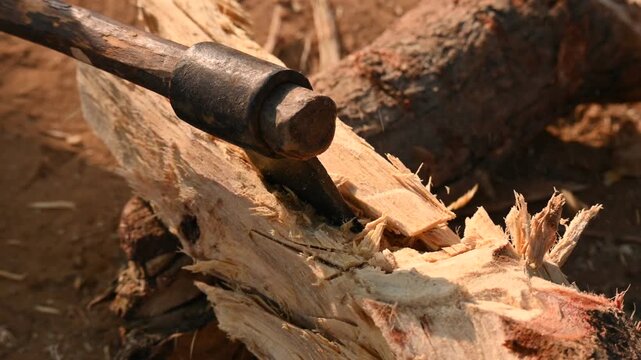 A person using a traditional hand axe to hew a rough wooden log resting. Traditional manual wood-chopping axe with a metal head and wooden handle. Its Commonly used in rural and village settings.