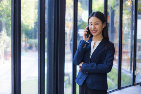 Businesswoman talking on smartphone near office window with confident smile