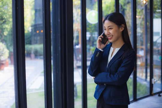 Businesswoman talking on smartphone near office window with confident smile