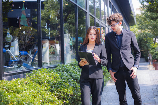 Business colleagues reviewing documents on tablet while walking outside office building