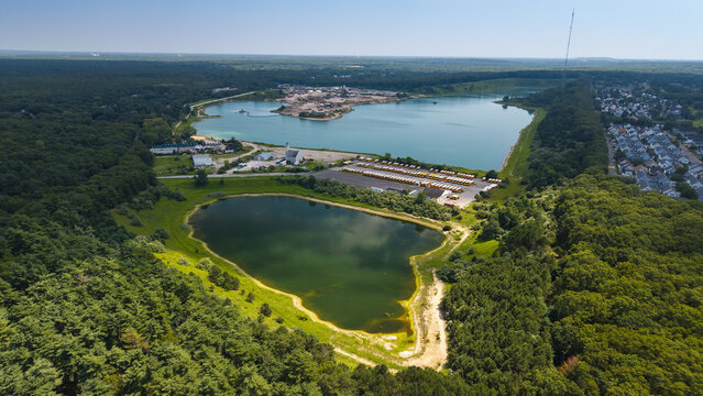 Aerial view of the gravel factory situated between two lakes, surrounded by dense forest and a parking lot filled with yellow school buses in Middle Island, New York, United States.