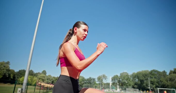 A young athletic girl in sportswear prepares for a workout at the stadium and warms up on the running tracks on a sunny summer day