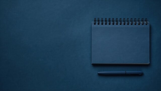 Dark blue spiral notebook and pen on solid blue background