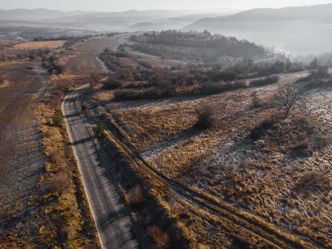 Aerial drone view of a winding road through a frosted hilly countryside landscape with morning fog