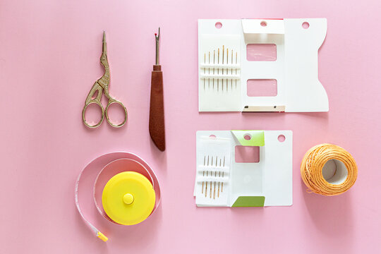 Sewing kit with scissors, seam ripper and thread spool on pink background