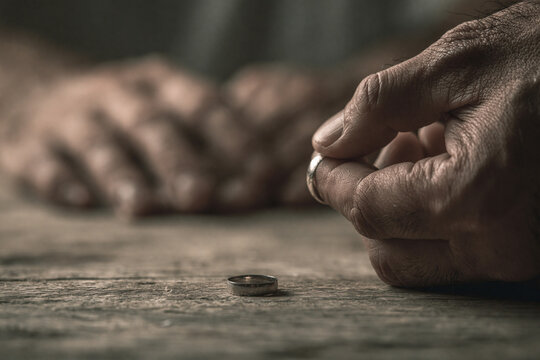 A pair of hands on a wooden table; one hand is removing a wedding ring, concept for couple problems.