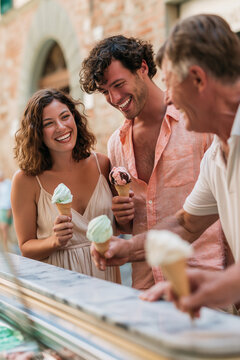 A candid, medium shot of a cheerful couple receiving gelato at a shop in Italy.