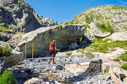 Female hiker crossing metal footbridge on mountain trail in alpine scenery
