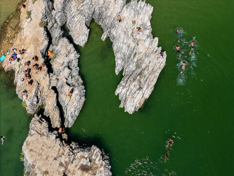 Aerial view of people swimming in green water and sunbathing on rocky cliffs in Cascais, Lisbon, Portugal.