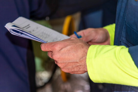 Close-up of a worker's hands holding a document, with workwear sleeves visible, representing professional work, documentation and routine activities in an industrial or maritime environment.
