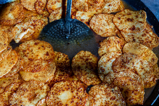 Traditional Indian Malpua Sweet Pancakes Frying In Pan. Closeup of golden brown malpua pancakes being deep fried and soaked in sugar syrup with a slotted spoon on an Indian street food night market