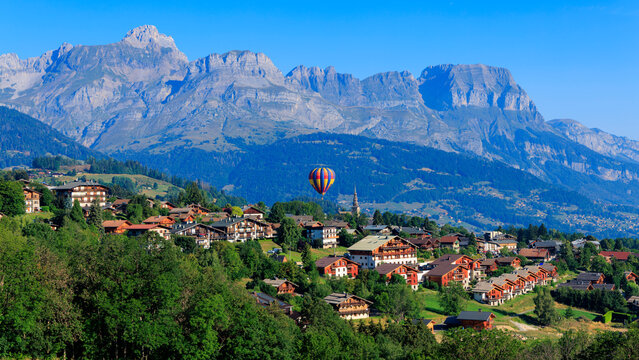 Hot air balloon flying over alpine village chalets and majestic mountain range in France