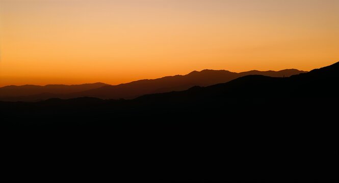 Silhouette lingers ridge rim amber wash drapes contours mellow glow settles chest steadying breath concept as Fading orb dips horizon pigments soften air warms quiet lull sweeps sinew easing tense fib