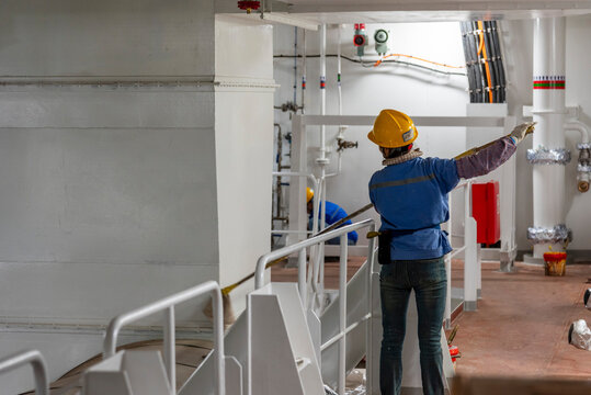 Shipyard employee carrying out cleaning and painting work as part of the finishing process on a newly constructed ship.