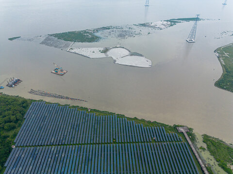 Aerial view of Sirajganj Power Station featuring extensive solar panel arrays along the riverbank with transmission towers and a dredging barge Sirajganj District, Rajshahi Division, Bangladesh.