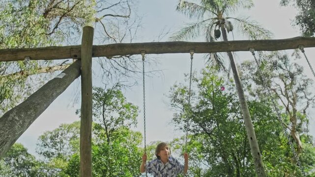 Happy teen boy on a swing in a park on a nice summer day. Adorable smiling child on a playground swinging on a swing on a warm summer day. Caucasian child enjoying his time outdoors on the playground.