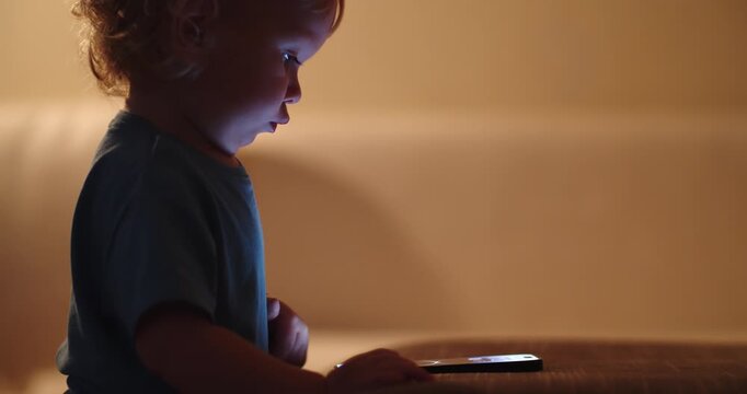 Child presses on the mobile phone screen, soft focus. Small baby presses by finger on the touch screen of the phone, close-up.  Little child learns to use modern technologies. Baby and cellphone.