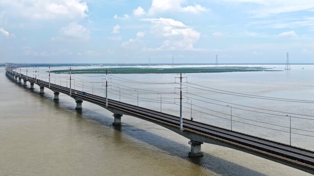 Aerial view of the Jamuna Bridge spanning the Jamuna River, with its long concrete structure, power lines, and surrounding water in Tangail District, Dhaka Division, Bangladesh.