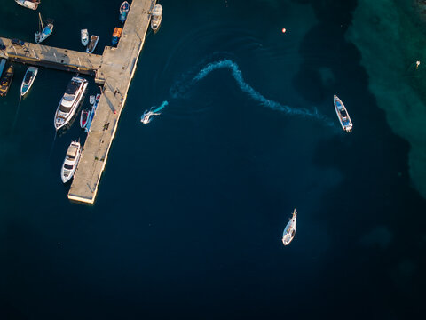 Aerial view of a pier with moored boats and a small motorboat creating a wake in the deep blue water of Porto Palermo, Qarku i Vlores, Albania.