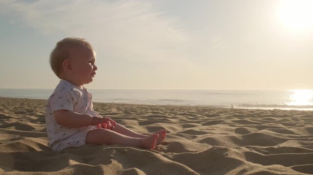 Little boy exploring the world on sand beach against  a blue ocean. Active, cheerful toddler plays along a sandy sea beach on sunny summer day. Slow motion: Baby is playing on the sea beach at sunset.