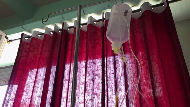 Low Angle View of Finished IV Saline Bottle hanging on Metal Stand against Red Curtains: A Stark Visual Metaphor for Completed Medical Treatment, Patient Recovery Milestones, and Healthcare Discharge
