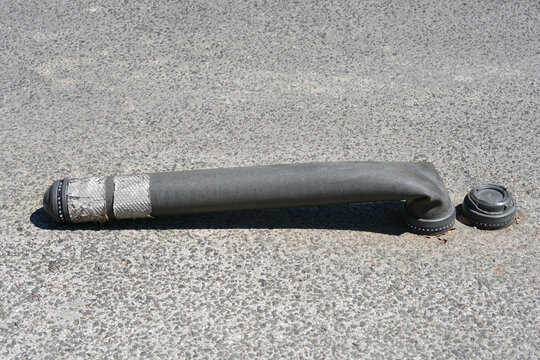 High angle view of a dark gray flexible rubber traffic bollard bent down on an asphalt road surface.