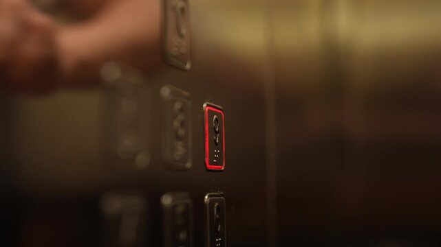 Female hand with fresh French manicure pressing illuminated call button on modern elevator panel, with reflection visible on shiny metallic surface, close-up, slow motion.