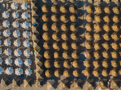 Aerial view of Llamani Beach featuring rows of straw umbrellas and white sunshades on the sandy shore in Himare, Vlore County, Albania.