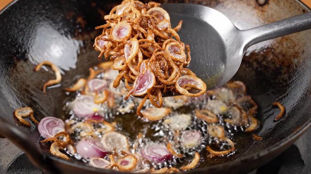 Sizzling Deep-Fried Shallots: Sliced red onions frying in hot oil inside a dark wok, ideal for culinary tutorials.
