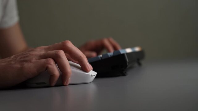 Male hands using white wireless computer mouse and mechanical keyboard on gray desk, symbolizing office work, remote freelancing, e learning, intense video gaming sessions. Shooting in slow motion.