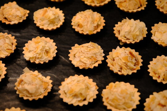 High-angle view of mini almond tarts topped with sliced almonds arranged on a black background.