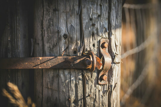 A weathered wooden fence post with a rusted metal latch and hinge mechanism captured in a close up shot with soft natural lighting and depth
