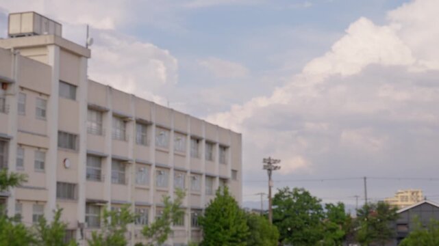 柔らかい光に包まれる夕暮れ時の校舎と背後で湧き上がる大きな入道雲のアウトフォーカス映像