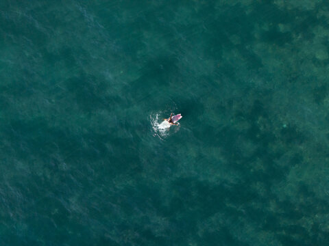 Aerial view of a lone surfer on a surfboard in the clear turquoise waters of Nusa Dua Beach in South Kuta, Bali, Indonesia.