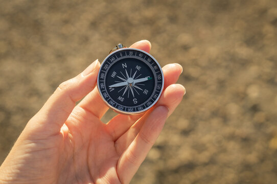 Hand holding a magnetic compass outdoors, symbolizing navigation, orientation and finding the right direction. Travel, adventure, decision making and business strategy concept with copy space.