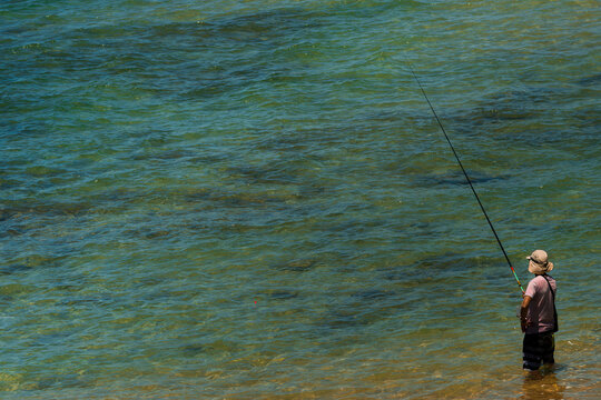 Fisherman standing in clear turquoise sea water holding a long fishing rod