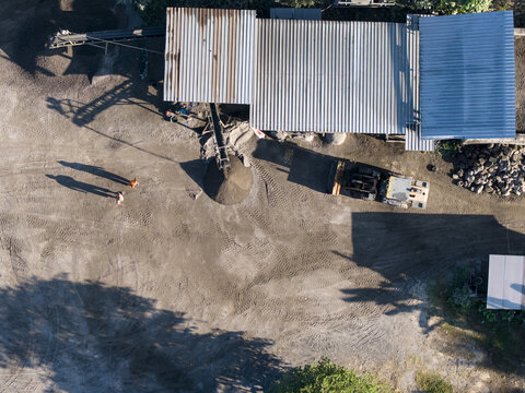 Aerial view of stone crushing facility with conveyor belt, heavy machinery, and workers on site in Kecamatan Karangnongko, Jawa Tengah, Indonesia.