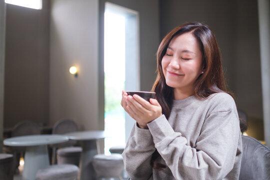 Portrait image of a woman with closed eyes holding and drinking hot coffee in cafe