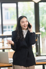 Fototapeta premium happy young Asian businesswoman talking on her smartphone and smiling while working in a modern office.