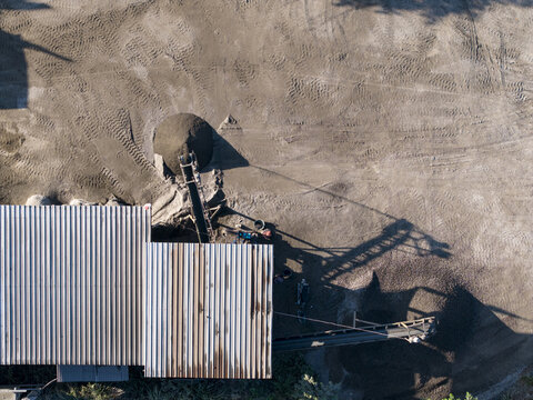 Aerial view of stone crushing facility with conveyor belts, piles of sand and gravel, and a corrugated metal roof structure in Kecamatan Karangnongko, Jawa Tengah, Indonesia.