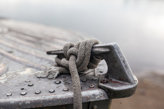 Close-up view of a weathered metal cleat with a rope knot secured tightly, situated on a boat dock with calm water in the background